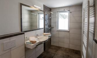 A modern bathroom with bright tiles and large mirrors. It features a shower and a window that lets in daylight.