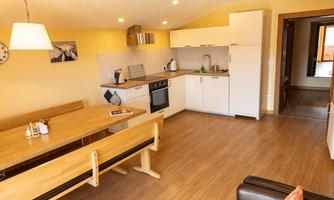 A modern kitchen with a wooden dining area and a cozy sofa. The walls are painted in warm colors and there is plenty of natural light.