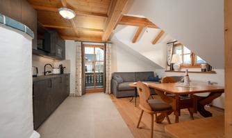 A modern and cozy kitchen living area with a wooden beam ceiling. The room is bright and inviting, with a dining table and a comfortable sofa.