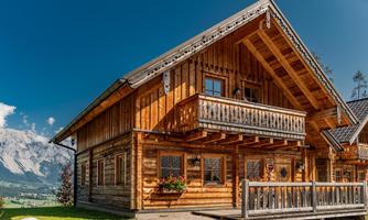 A traditional wooden house with a balcony and beautiful views. The surroundings show tall mountains and green grass.