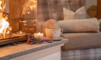 A cozy living room scene with an open fireplace and a comfortable sofa. On the table are a cup of tea, a candle, and lavender.