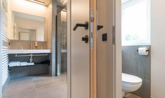 A modern bathroom with a shower, a toilet, and a large mirror. The room design is bright and friendly.