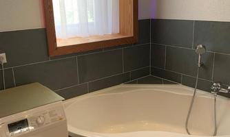 A bathroom with a modern washing machine and an elegant bathtub. The large window lets in plenty of natural light.