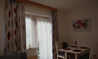 A cozy dining area with a table and chairs. Generous windows with curtains let in plenty of light.