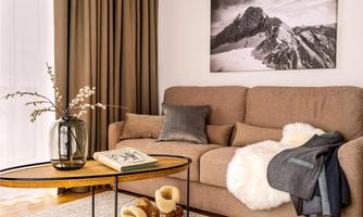 A cozy living room with a beige sofa and a round coffee table. A picture of majestic mountains hangs on the wall.
