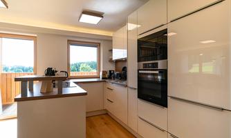 A modern kitchen with white cabinets and wood details. Large windows provide plenty of daylight and a view of the greenery.
