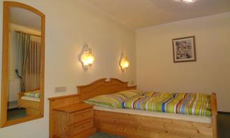 A cozy bedroom with a wooden bed and colorful bedding. There is a large mirror on the wall and a decorative wall lamp.