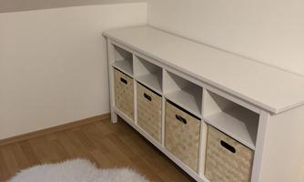 A bright room with a white piece of furniture and woven baskets. A soft, white rug lies on the floor.