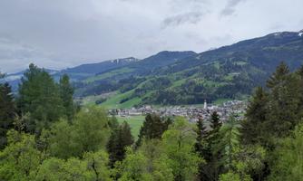 A picturesque view of a valley with green hills and forests. In the background, a small town and mountains can be seen.