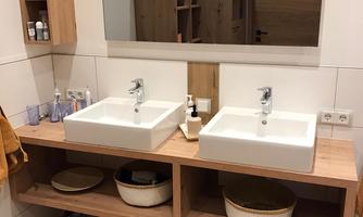 A modern bathroom with two sinks and a large mirror. The wooden vanity provides storage space and is equipped with decorative baskets.