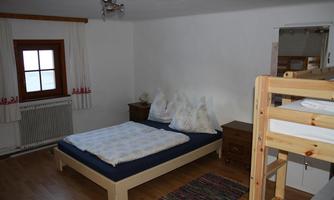A simple bedroom with a double bed and a loft bed. The walls are painted in neutral tones and there is natural light coming through a window.