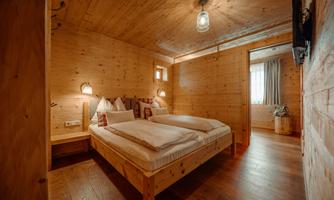 A modern wooden bedroom with two beds and soft lighting. Large space with windows that let in daylight.