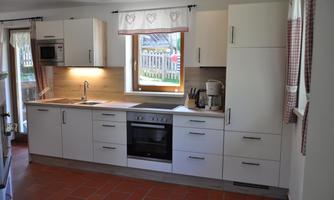 A modern kitchen with white cabinets and an oven. Windows with curtains let in plenty of light.