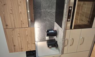 A modern kitchen with light wooden fronts and gray surfaces. The equipment includes a stove, an oven, a microwave, and electrical appliances.