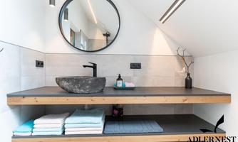 A modern bathroom with a wooden washbasin and a round mirror. Clean towels in various colors are laid out on the table.