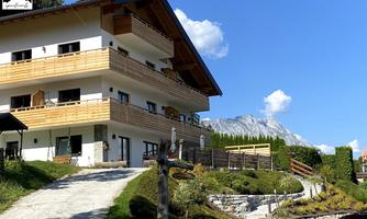 A modern building with wooden cladding in the mountains.  
Surrounded by green spaces and beautiful scenery.