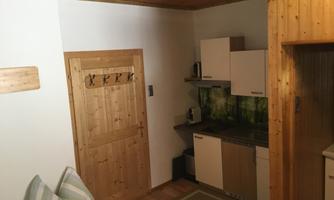 A small, cozy kitchen with modern furniture and wooden details. The walls are light, and there is a view of a wooden cupboard and a door.