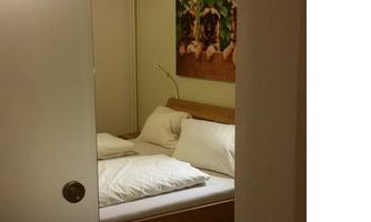 A simple bedroom with a double bed and white pillows. A colorful picture hangs on the wall.