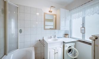 A modern bathroom with a bathtub and a sink. Additionally, there is a washing machine and plenty of natural light through the window.
