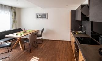A modern kitchen with a dining table and chairs. The room has a bright, inviting atmosphere with wooden flooring.