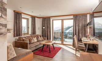 A modern living room with a cozy sofa and a dining table. Large windows offer a view of the mountains and provide plenty of daylight.