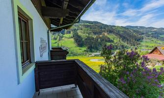 A balcony with a view of green hills and mountains. The sky is blue with a few clouds.