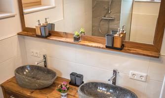 A modern bathroom with two elegant stone sinks. The wooden dresser and the large mirror give the room an inviting atmosphere.