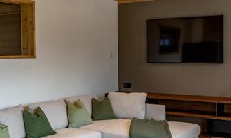 A modern living room with a comfortable sofa and green cushions. The wooden floor and the wooden beam ceiling give the room a cozy atmosphere.