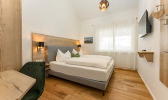 A modern bedroom with a large bed and elegant wooden decorations. There is a small desk and a television on the wall.
