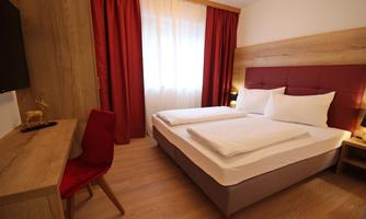 A modern bedroom with a double bed and wood-colored furnishings. The red curtain and a desk give the room a cozy atmosphere.