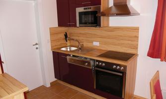 A modern kitchen with a combination of wood and burgundy furniture. It features a stove, an oven, and a sink.