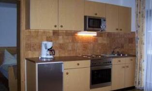 A modern kitchen with light wooden cabinets and an elegant tiled backsplash. It is equipped with a stove, microwave, and refrigerator.