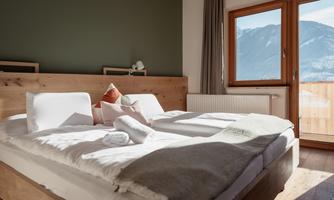 A beautiful, modern bedroom with a large bed and cozy bedding. Through the window, you can see the mountains and a blue sky.
