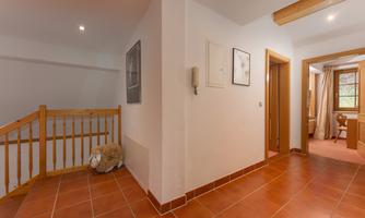 A bright hallway with a wooden lattice and terracotta-colored tiles. Pictures hang on the walls, and a door leads to another room.