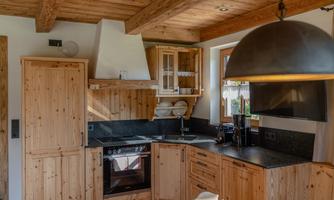 A modern kitchen with wooden cabinets and a black countertop. Large windows provide plenty of daylight.