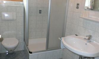 A modern bathroom with a shower, a sink, and a toilet. The walls are light tiled and there is a window that lets in natural light.