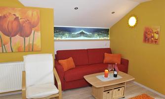 A cozy living room with a red sofa and a white chair. The walls are painted yellow, and decorations with floral motifs create an inviting atmosphere.