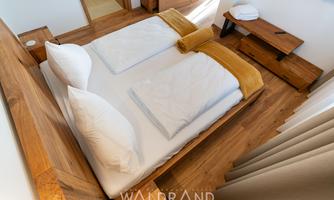 A stylish bedroom with a wooden double bed and white bedding. The warm color scheme and natural light create an inviting atmosphere.