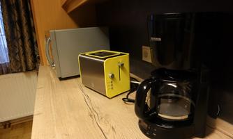 A modern kitchenette with a yellow toaster, a black coffee maker, and a microwave. The wooden table looks simple and functional.