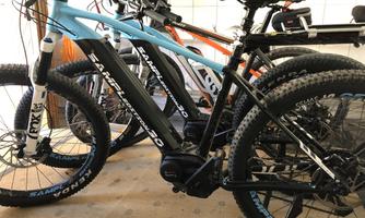 A couple of mountain bikes are in a room. The black e-mountain bike has a bluish-gray accent color and seems ready for a ride.