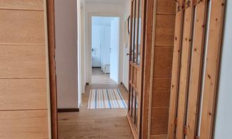 A bright hallway with wood paneling and a shoe rack. An open door design leads from the hallway into another room.
