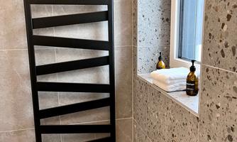 A modern shower area with a stylish black towel heater. Bright tiles and a windowsill with care products and fresh towels complete the picture.
