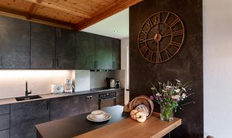 A modern kitchen with dark cabinets and a wooden kitchen table. A large clock hangs on the wall, and a bouquet of flowers adds a beautiful accent.