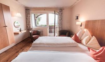 A cozy bedroom with two beds and bright decorations. Large windows provide a view outside and let in plenty of light.