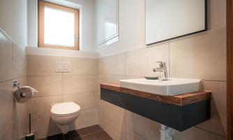 A modern bathroom with a minimalist design. It features a sink with a wooden shelf, a toilet, and a window.