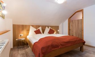 A cozy bedroom with a large bed and red bedding. The walls are bright and the decor is modern and inviting.