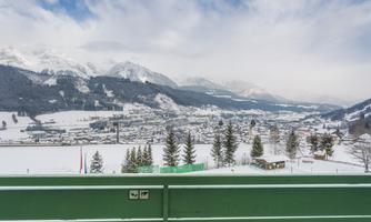 A picturesque snow landscape with a view of a small village in the Alps. In the background, snow-capped mountains rise under a cloudy sky.