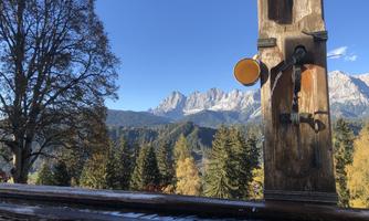A wooden sculpture with a faucet and a view of majestic mountains. In the background, there are trees and a clear blue sky.