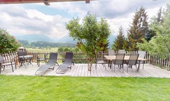 A cozy terrace with lounge chairs and a table for four people. In the background, you can see a beautiful landscape with mountains and trees.