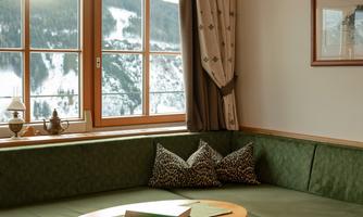 A cozy room with a green sofa and a round table. The windows offer a beautiful view of the mountains.
